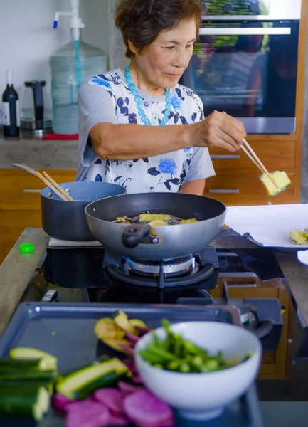 lifestyle portrait of senior happy and sweet Asian Japanese retired, woman cooking at home kitchen alone neat and tidy enjoying preparing meal in elderly and mature home cook concept