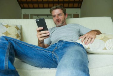 yaşam tarzı kapalı genç mutlu ve çekici portresi adam evde kanepe koltuk rahat ve neşeli modern daire cep telefonu ağ üzerinde Internet Sosyal medya app'ı kullanarak