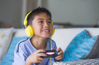 Genç İspanyol küçük çocuk heyecanlı ve mutlu online video oyun denetleyicisi zevk sahip holding kulaklık ile oynarken portresi eğlenceli oyun duygu ve çocuk oyun bağımlılığı kanepede oturan