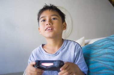 Eğleniyor zevk Latin Genç çocuk 8 yaşında heyecanlı ve mutlu oyun video oyunu online holding uzaktan kumanda portresi yaşam tarzı internet oyun çocuk bağımlılığı koltukta oturan