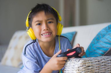 Genç Latin küçük çocuk portresi yaşam tarzı heyecanlı ve mutlu oyun video oyun online ile eğleniyor denetleyicisi tutan kulaklık oyun duygu kanepede oturup oyun bağımlılığı evlat