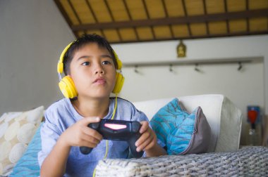 Genç Latin küçük çocuk portresi yaşam tarzı heyecanlı ve mutlu oyun video oyun online ile eğleniyor denetleyicisi tutan kulaklık oyun duygu kanepede oturup oyun bağımlılığı evlat