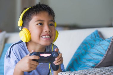 Genç Latin küçük çocuk portresi yaşam tarzı heyecanlı ve mutlu oyun video oyun online ile eğleniyor denetleyicisi tutan kulaklık oyun duygu kanepede oturup oyun bağımlılığı evlat
