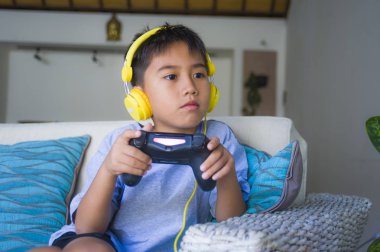 yaşam tarzı portre Latin genç çocuğun heyecanlı ve mutlu online video oyun denetleyicisi zevk sahip holding kulaklık ile oynarken eğlenceli çocuk oyun duygu ve bağımlılığı kanepede oturan