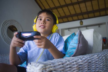 Latin küçük çocuk heyecanlı ve mutlu online video oyun denetleyicisi zevk sahip holding kulaklık ile oynarken portresi yaşam tarzı çocuk oyun duygu ve bağımlılığı kanepede oturan eğlenceli