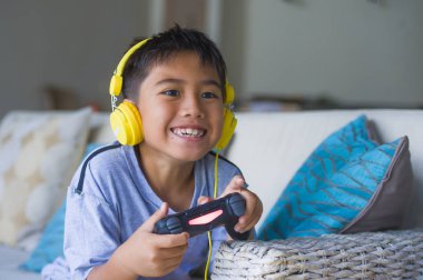 Latin küçük çocuk heyecanlı ve mutlu online video oyun denetleyicisi zevk sahip holding kulaklık ile oynarken portresi yaşam tarzı çocuk oyun duygu ve bağımlılığı kanepede oturan eğlenceli