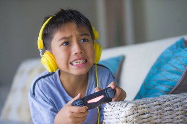 Latin küçük çocuk heyecanlı ve mutlu online video oyun denetleyicisi zevk sahip holding kulaklık ile oynarken portresi yaşam tarzı çocuk oyun duygu ve bağımlılığı kanepede oturan eğlenceli