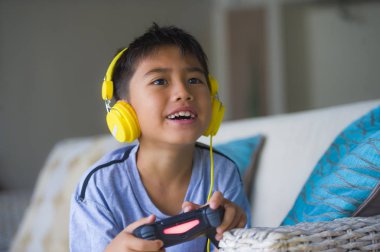 Genç İspanyol küçük çocuk heyecanlı ve mutlu online video oyun denetleyicisi zevk sahip holding kulaklık ile oynarken portresi eğlenceli oyun duygu ve çocuk oyun bağımlılığı kanepede oturan