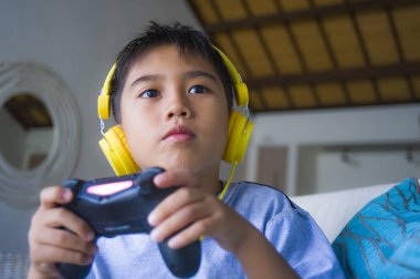 Genç İspanyol küçük çocuk heyecanlı ve mutlu online video oyun denetleyicisi zevk sahip holding kulaklık ile oynarken portresi eğlenceli oyun duygu ve çocuk oyun bağımlılığı kanepede oturan