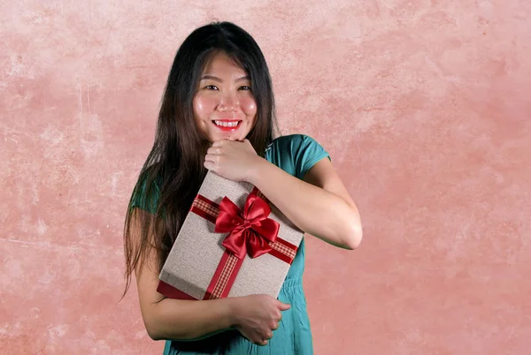 isolated pink  background portrait of young happy and beautiful Asian Chinese woman holding gift box receiving  birthday or Christmas present holding the parcel smiling cheerful