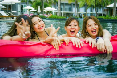 lifestyle portrait of young Asian Chinese and Korean women group of friends , attractive girlfriends at holidays resort swimming pool having fun in airbed smiling cheerful and happy enjoying together clipart
