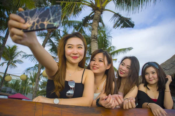lifestyle portrait of group with young happy and attractive Asian Chinese and Korean women hanging out , girlfriends enjoying holidays trip in tropical resort taking selfie picture with mobile phone