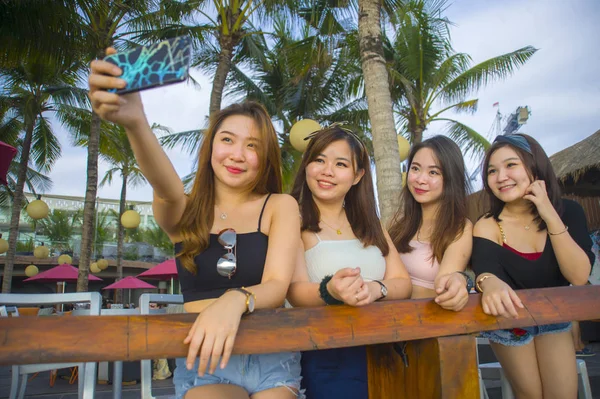 lifestyle portrait of group with young happy and attractive Asian Chinese and Korean women hanging out , girlfriends enjoying holidays trip in tropical resort taking selfie picture with mobile phone