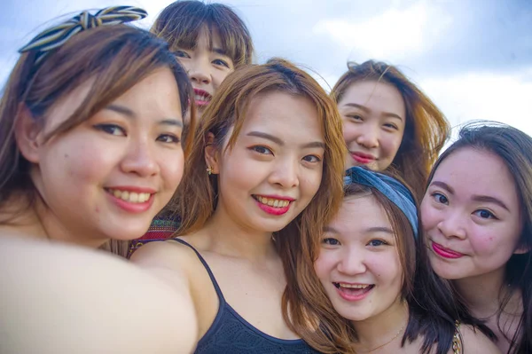 lifestyle beach portrait of Asian Korean and Chinese women, group of happy beautiful young girlfriends taking selfie picture together with mobile phone smiling cheerful enjoying girls holidays trip