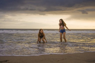 iki Asyalı Çinli Kadınlar mutlu ve çekici genç kız ya da kız kardeşi deniz günbatımı plajda oynayan ışık yaz tatili zevk güzel eğleniyor seyahat birlikte kaygısız