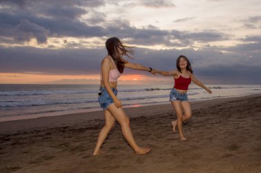kaygısız ve neşeli yaşam tarzı açık havada dikey iki mutlu genç kız kardeşi veya Asyalı Çinli kız ile birlikte yaz tatil gezisi zevk eğleniyor onun en iyi arkadaşı günbatımı Plajı'nda oynarken