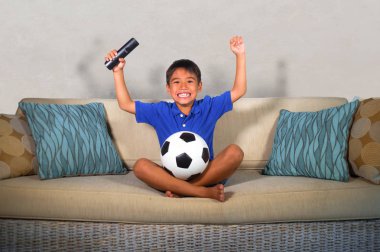 lifestyle portrait of young hispanic boy happy and excited watching football game on television at home living room couch celebrating scoring goal gesturing cheerful as kid soccer crazy fan  clipart
