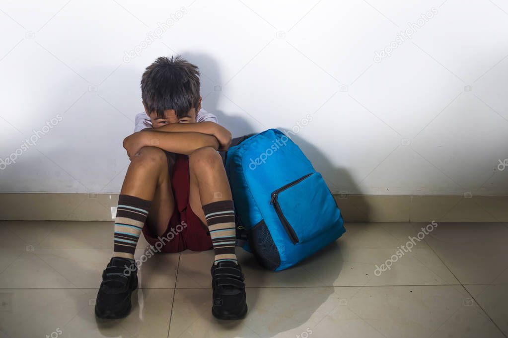 lifestyle dramatic bullying victim portrait of young sad scared latin kid 8 years old in school uniform and backpack sitting alone crying depressed and frightened suffering abuse being bullied