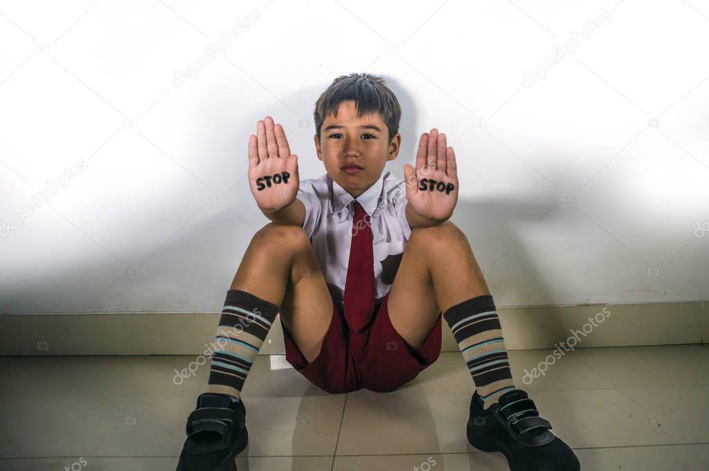 lifestyle dramatic isolated portrait of young kid sad and depressed suffering bullying problem and abuse at school with stop word written on his hands feeling helpless in bullied child victim