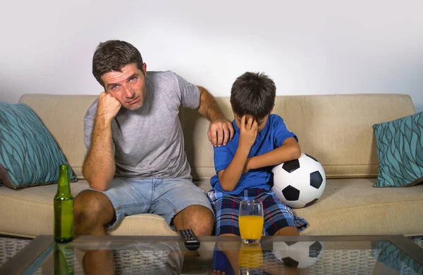 young father and little son watching football together at home couch feeling frustrated and sad with their team defeated losing the game in kid and dad dejected soccer fans concept