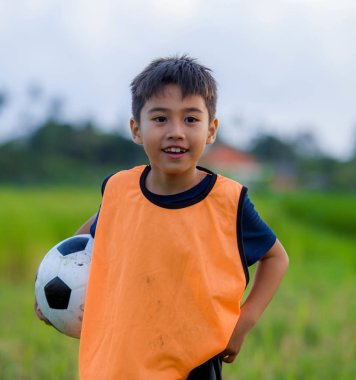 yaşam tarzı yeşil çim alan gülümseyen neşeli giyen eğitim yeleğe çocuk eğitim spor kavramı, açık havada futbol futbol topu tutan mutlu ve yakışıklı genç çocuk portresi