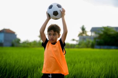 yaşam tarzı yeşil çim alan gülümseyen neşeli giyen eğitim yeleğe çocuk eğitim spor kavramı, açık havada futbol futbol topu tutan mutlu ve yakışıklı genç çocuk portresi