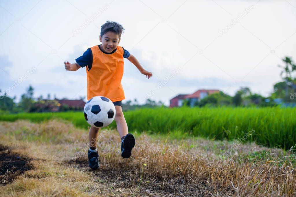 8 or 9 years old happy and excited kid playing football outdoors in garden wearing training vest running and kicking soccer ball , the kid having fun practicing sport 
