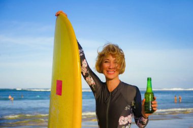 yaz tatil tropikal Beach serin mayo oynak denizde giymiş zevk neşeli içki bira şişesi gülümseyen sarı sörf tahtası tutan genç seksi güzel ve mutlu sörfçü kadın