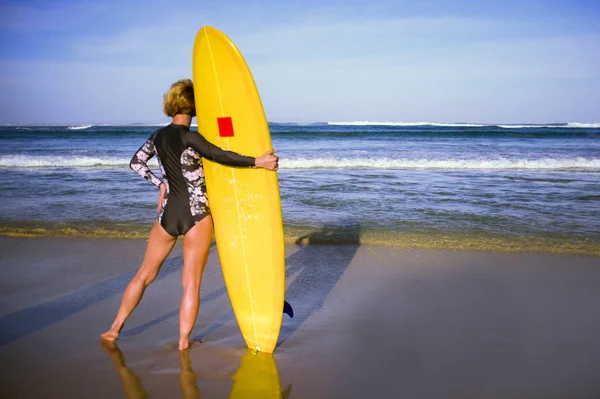 年轻的迷人和运动的冲孩的背部视图在沙滩上举行黄色冲浪板看在蓝色海 在夏天冲浪假期和生活方式概念 — 图库照片