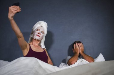 komik yaşam tarzı makyaj yüz maskesi ve çaresiz yüz ifadesi ile yatakta ve kocası selfie garip adam kadın ilişki kavramı içinde alarak havlu ile eksantrik ev kadını portresi