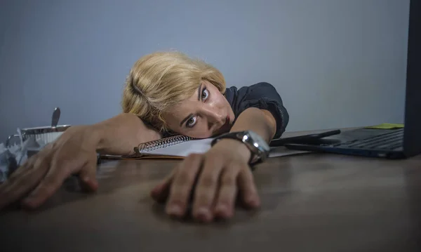 young beautiful depressed and sad blonde woman working with laptop computer feeling tired leaning low at office desk overwhelmed by paperwork suffering depression and job stress
