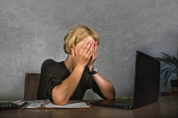 young frustrated and stressed business woman crying sad at office desk working with laptop computer overwhelmed by paperwork workload covering her face desperate suffering depression