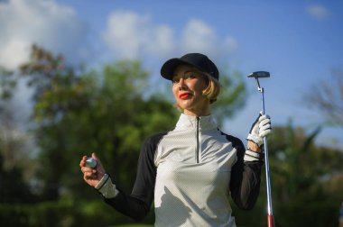 Genç güzel ve gülümseyen topu ve atıcı Kulübü neşeli yeşil koymak arka plan üzerinde izole şık Golf giysileri tutan golf oynarken mutlu kadın yaşam tarzı açık havada portre 