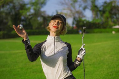 Genç güzel ve gülümseyen topu ve atıcı Kulübü neşeli yeşil koymak arka plan üzerinde izole şık Golf giysileri tutan golf oynarken mutlu kadın yaşam tarzı açık havada portre 