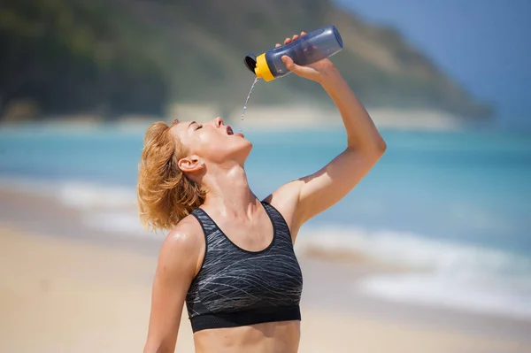 若い幸せと魅力的なスポーツ ランナー女性飲料水ボトルや健康的なライフ スタイルのコンセプトでフィット感と運動体を示す熱帯の楽園浜でワークアウトを実行した後のスポーツド リンク — ストック写真