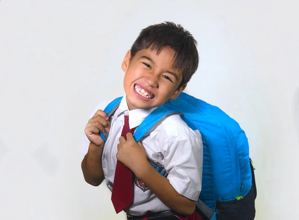 7 or 8 years old sweet kid in uniform carrying bag full of books feeling upset and complaining about the weight of the backpack in lazy schoolboy unhappy about going back to school