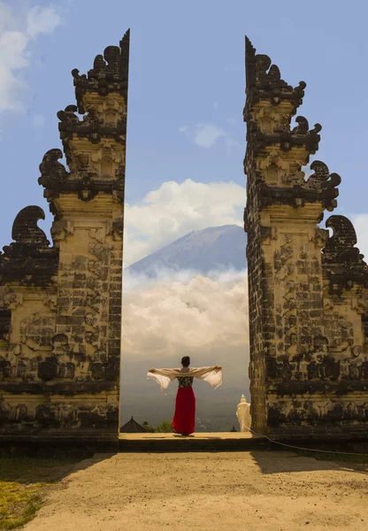 Asian woman spreading arms in front of Bali volcano Mount Agung through the beautiful and majestic gate of the hindu Pura Lempuyan temple of Indonesia in Asia holidays travel destination