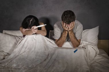 young couple in bed scared and stressed after positive result on pregnancy test with pregnant woman expecting unwanted baby and man feeling overwhelmed worried and disappointed  clipart