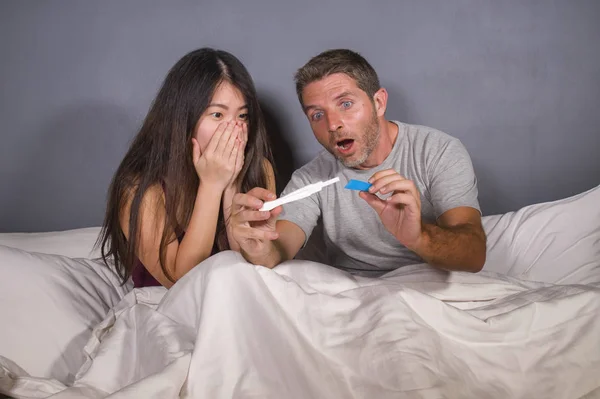 young beautiful and stressed couple in bed looking pregnancy test feeling happy and surprised by positive pregnant result looking excited and scared about expecting a baby