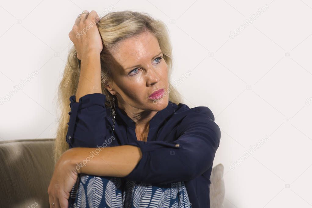 40s depressed and anxious beautiful blonde woman suffering depression feeling frustrated and lonely sitting at home sofa couch thoughtful and pensive in middle age crisis and life problem 
