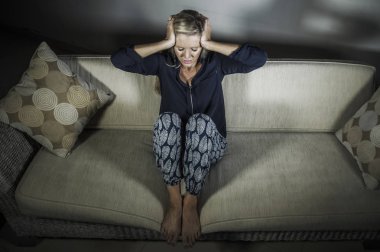 40'lı depresif ve depresyon ve baş ağrısı duygu endişeli güzel sarışın kadın evde kanepe koltuk üzgün ve umutsuz orta yaş krizi ve yaşam dramatik sorunu içinde oturan boşa 