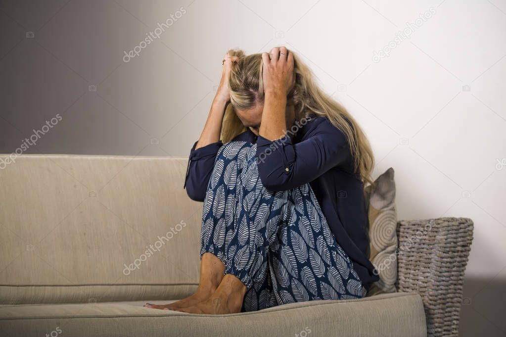 40s depressed and anxious beautiful blonde woman suffering depression and anxiety crisis feeling frustrated and thinking lonely at home sofa couch looking helpless in pain and desperate