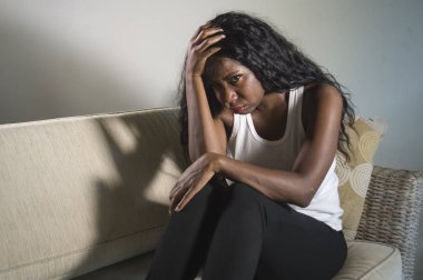 genç çekici ve üzgün oturan siyah Afrikalı-Amerikalı kadın evde kanepe depresif duygu endişeli ve sinirli sorun depresyon ve anksiyete krizi ya da korkunç baş ağrısı acı kanepe