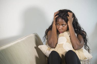 adet adet ağrısı üzgün seyir yastık tutan genç çekici ve üzgün oturan siyah Afrikalı-Amerikalı kadın evde kanepe depresif duygu endişeli ve sinirli kanepe acı