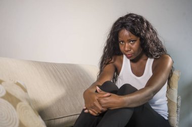 genç çekici ve üzgün oturan siyah Afrikalı-Amerikalı kadın evde kanepe depresif duygu endişeli ve sinirli sorun depresyon ve anksiyete krizi ya da adet ağrısı acı kanepe
