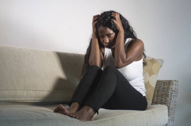 genç çekici ve üzgün oturan siyah Afrikalı-Amerikalı kadın evde kanepe depresif duygu endişeli ve sinirli sorun depresyon ve anksiyete krizi ya da korkunç baş ağrısı acı kanepe