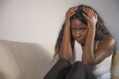 genç çekici ve üzgün oturan siyah Afrikalı-Amerikalı kadın evde kanepe depresif duygu endişeli ve sinirli sorun depresyon ve anksiyete krizi ya da korkunç baş ağrısı acı kanepe