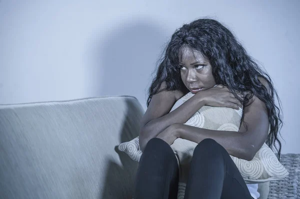 young attractive and sad black African American woman sitting depressed at home sofa couch feeling anxious and frustrated suffering menstruation period pain holding pillow looking upset