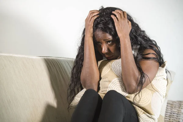 年轻的迷人和可悲的黑人非洲裔美国妇女坐在沮丧的家庭沙发沙发上感到焦虑和沮丧的月经期疼痛抱枕看着心烦 — 图库照片