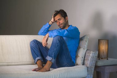 genç çekici ve yakışıklı yaşam tarzı portre üzgün oturan latin adam yorgun ve evde depresif duygu koltuk kanepe boğulmuş ve depresyon anksiyete ve kriz sorun acı endişeli
